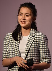 Front view of a smiling Chantel Yiu, as she is looking away from the camera, wearing a plaid blazer with a white undershirt
