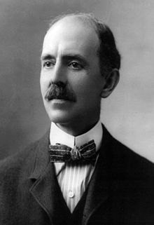 Balding white man with a dark mustache in a dark suit