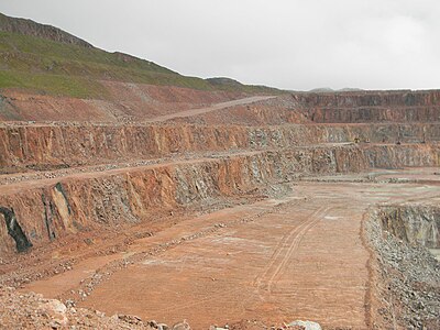 Der riesige Steinbruch bei Glensanda im Glensanda-Granodiorit. Links im Vordergrund steilstehende dunkle Appinitbänder. Auffallend die rote Gesteinsfärbung.