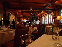 table-height view of white tablecloths, windows at right, empty glassware, dark with warm lighting