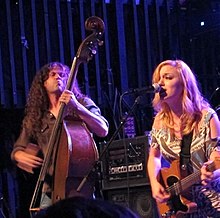 Lydia Loveless singing into a microphone and playing guitar while Ben Lamb plays a stand-up bass.