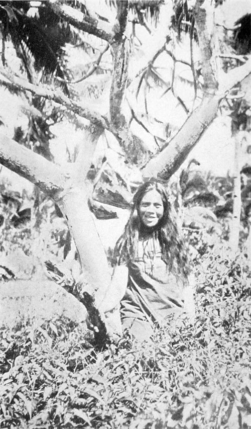 A photo of a woman posing and smiling next to a tree