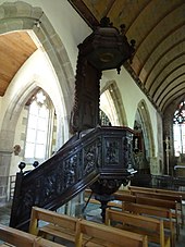 Photographie montrant une chaire à prêcher sculptée en bois foncé dans la nef d'une église