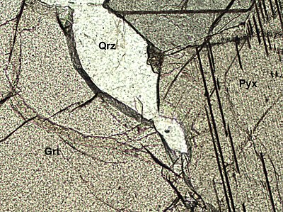 Dünnschliff, der einen Quarz (Qrz), einen Granat (Grt) und ein Pyroxen (Pyx) zeigt. Der Quarz hat dieselbe Lichtbrechung wie das Einbettungsmedium (1,54) und zeigt daher nur ein geringes Chagrin. Der Granat besitzt eine sehr hohe Lichtbrechung (um die 1,8), die in einem hohen Chagrin resultiert. Minerale der Pyroxengruppe besitzen eine niedrigere Lichtbrechung als der Granat und haben daher auch ein schwächeres Chagrin. Bildhöhe ca. 1 Millimeter.