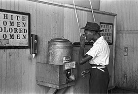 An African-American man drinking from a racially segregated water cooler marked "Colored", in Oklahoma City c. 1939 "Colored" drinking fountain from mid-20th century with african-american drinking.jpg