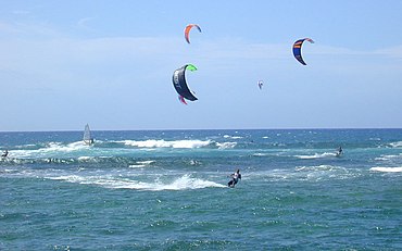 Kite surfing off in strong onshore winds off the north shore of O‘ahu in Hawai‘i. Note the wind-surfer catching the wave break.