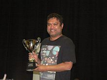 Paul Sinha holding the Fighting Talk Champion of Champions Trophy.jpg