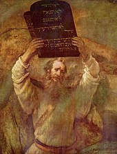 This is an image of an oil on canvas picture by Rembrandt (1659) of a bearded man representing Moses with two tables of stone of the ten commandments held high in both hands.