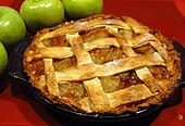 An apple pie on a red table cloth, with green apples next to it.