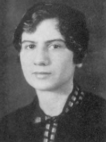 A young white woman with short dark curly hair, wearing a dark blouse