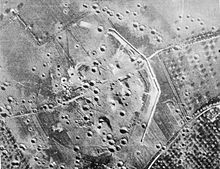 Photo aérienne en noir et blanc d'un terrain constellé de cratères, où l'on distingue des restes de structures militaires.
