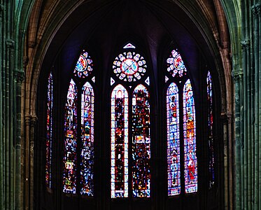 Vue depuis la nef des verrières des fenêtres hautes du chœur. L'image est sombre et de mauvaise qualité. Sont cependant visibles, sur la seconde fenêtre en partant de la droite, quatre hommes portant des auréoles. De part et d'autre des verrières, des piliers de la nef sont visibles.
