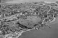 Tønsberg med Slottsfjellet, det viktigste landemerket i byen, sett fra nordøst, på flyfoto tatt av Widerøe i 1957. Bildet viser sentrum og Haugar med Tønsberg sjømannsskole, nå Haugar Vestfold Kunstmuseum, oppe til høyre, bak i bildet. Foto: Vestfoldmuseene