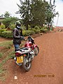 A taxi motorcyclist with his engine on a red dirt road, Kigali.