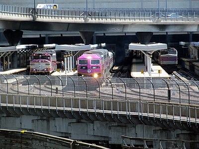 A diesel locomotive with a passenger train leaving a station with several tracks and high-level platforms