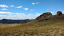 Small, rocky hills interspersed above a flat landscape with bushes