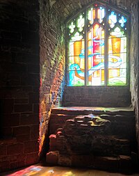 An stained glass window, with three columns and some curved pieces of glass at the top, surrounded by blackness. A blue river traces its way through the glass, surrounded by yellow, orange and red background glass.