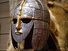 Photo d'un casque couvrant visage et oreilles aux motifs ciselés représentant des scènes de guerre