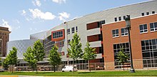 Four story brick and steel building before blue sky and clouds with trees and grass in foreground