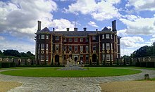 A photograph of the front of the house, showing a brick building with a circular drive in front of it