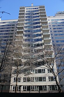 One of Manhattan House's wings as seen from ground level. The wing protrudes from the main portion of the building. The facade is made of white brick, with glass windows, and there are balconies on several stories.