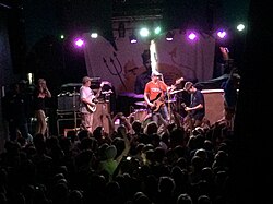 Image of a concert with an audience and the band Modern Baseball both shown