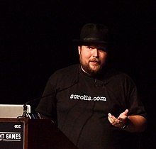 Notch speaking at GDC 2011, in front of a computer and wearing a fedora.