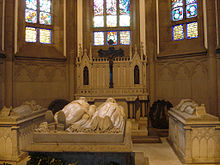 Inside a gothic chapel, a marble effigy of a bearded emperor in uniform and his wife lies atop an intricately carved stone sarcophagus