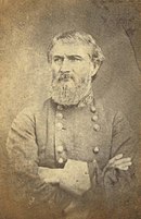 Sepia tone photo shows a bearded man with his arms crossed. He wears a gray military uniform with two rows of buttons.