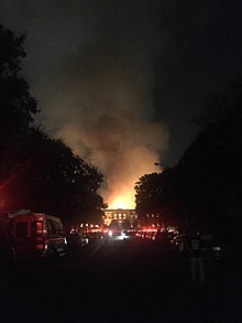 Bức ảnh của ngọn lửa từ viện bảo tàng làm sáng bầu trời đêm ở cuối một con đường tối, hai bên là xe cộ đỗ