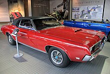 Vue de trois quarts avant droit, voiture rouge à toit noir, dans une salle d'exposition. Porte-skis à l'arrière.