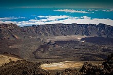 Vue de parois rocheuses depuis une zone plus haute, avec la mer et des nuages en arrière-plan.