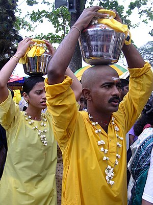 Worshippers carry heavy pots in a procession d...