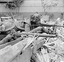 Lance Corporal R. Hearn and Private F. Slater (nearest camera) of the 1st Battalion, Royal Norfolk Regiment aim their weapons in the ruins of Kervenheim, 3 March 1945. Corporal Hearn is using a captured German MP40 'Schmeisser' submachine gun. The Campaign in North West Europe 1944-45 B15048.jpg