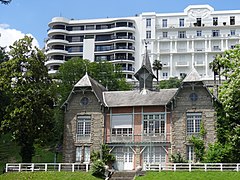 Photographie en couleurs d'une villa dont la toiture porte un clocheton central ; immeuble moderne en arrière-plan.