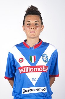 Woman with black hair in blue and white football kit.