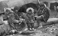 Inuitfamilie 1917 i tradisjonelle drakter av skinn og med et lite barn i skinnpose på ryggen. Foto: National Geographic Magazine