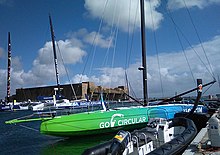 Voilier vert et bleu vu de trois quarts avant, amarré au ponton.