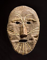 A simple oval-shaped hide mask with small oval holes for eyes and mouth. Strips of contrasting hide form facial markings, eyebrows, and a nose.