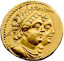 A gold coin shows paired, profiled busts of a plump man and woman. The man is in front and wears a diadem and drapery. It is inscribed "ΑΔΕΛΦΩΝ".