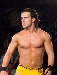 Adult white male wearing yellow trunks with long hair staring at the crowd during a wrestling event