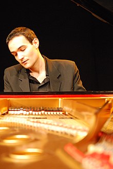 Un homme devant un piano à queue, concentré, les yeux fermés