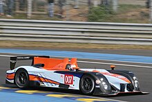 Photographie d'une voiture de sport-prototype, bleu ciel, orange et noir, vue de trois-quart avant, sur une piste