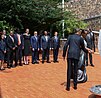 Rechts im Bild halten Paul und Jeannette Kagame wohl eine Fackel in eine Richtung, die nicht mehr im Bild ist. In wenigen Metern Abstand hinter ihnen stehen eine Reihe Personen in dunklen Anzügen und Kleidern und sehen ihnen zu.
