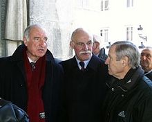 Trois hommes en costume cravate discutent à la sortie d'une église.