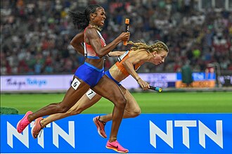 Alexis Holmes in rot-weiß mit Staffelstab in der Hand zieht an Femke Bol in Orange, die stolpert und die Kontrolle über den Staffelstab verliert, vorbei zu WM-Gold.