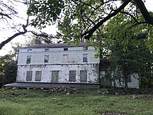 Фотография белого заброшенного дома в заросшем дворе.