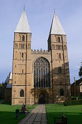 Простой нормандский западный фасад с двумя башнями, увенчанными короткими пирамидальными шпилями. Между башнями вставлено большое готическое окно.