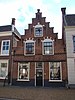 Huis met trapgevel met geblokte ontlastingsbogen, toppilaster, sierankers en schuiframen in stijl