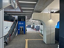 Under the viaduct with an escalator and lift up to the platform on the left